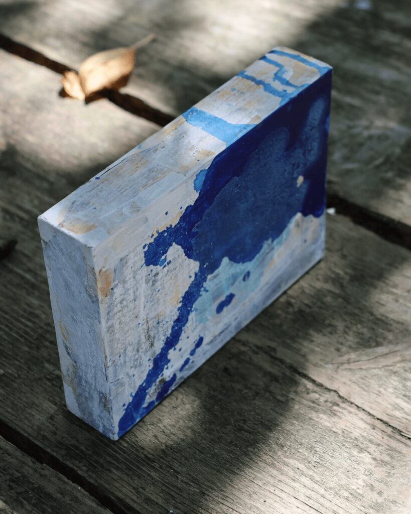 "Objects, No. 12," an angled perspective of a minimalist art object, showcasing the organic way that pools of dark and light blue paint flow over the block's rough, weathered white surface and around its edges. This view highlights the artwork's raw, tactile texture. This Wabi Sabi style piece is from the 'Objects' series by Asahi Tanaka.