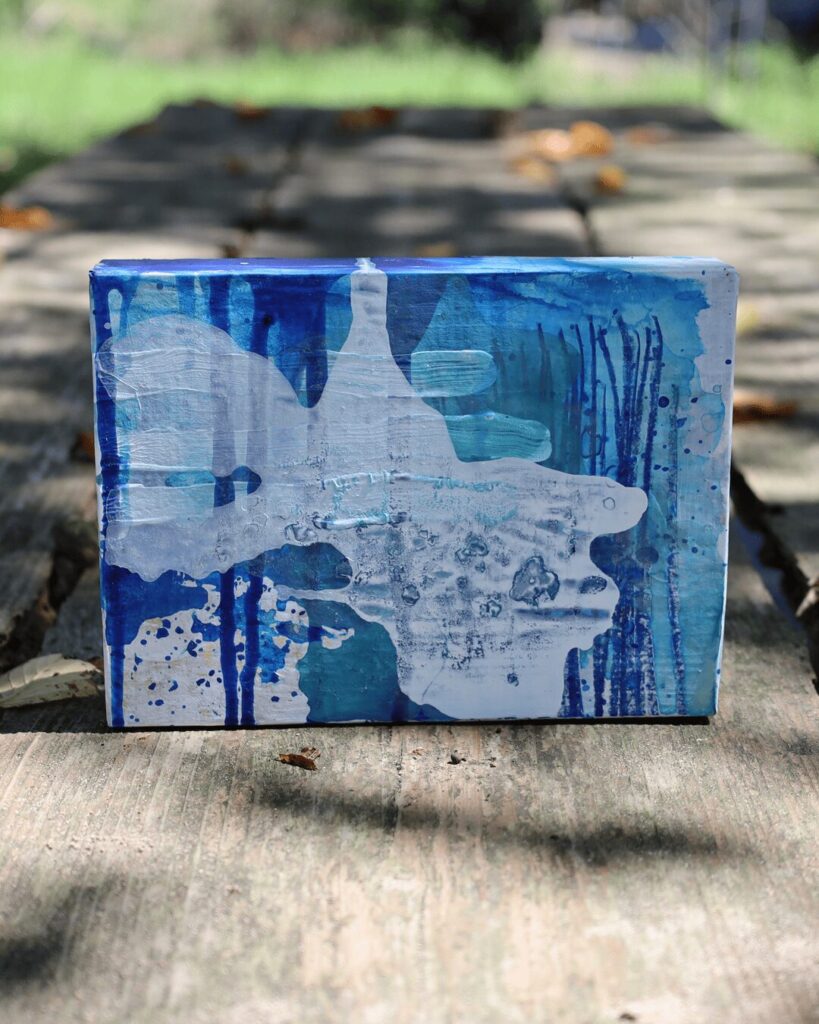 "Objects, No. 3," a frontal view of a deeply textured abstract art object, showcased in natural, dappled light. A gestural cascade of semi-opaque white paint serves as a veil, revealing intriguing glimpses of the energetic blue paint and crayon marks hidden beneath. This Wabi Sabi style artwork is from the 'Objects' series by Asahi Tanaka.
