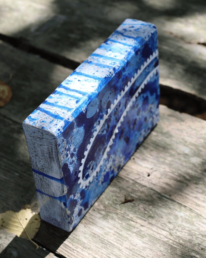 "Objects, No. 7," an angled view of a sculptural art object, highlighting how a unique, biomorphic white line wraps around the top and side surfaces. This intricate, gear-like pattern creates a striking graphic element over a deep and chaotic sea of layered blue paint. This piece is from the 'Objects' series by Asahi Tanaka.