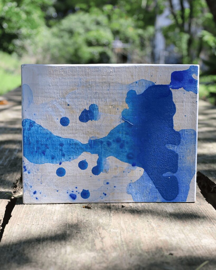 "Objects, No. 8," a serene frontal view of a minimalist abstract art block, resting on a rustic wooden plank. The composition is a quiet meditation on form, featuring a large, continent-like shape of deep blue paint and subtle splatters on a weathered, off-white surface. This piece of contemporary art is from the 'Objects' series by Asahi Tanaka.