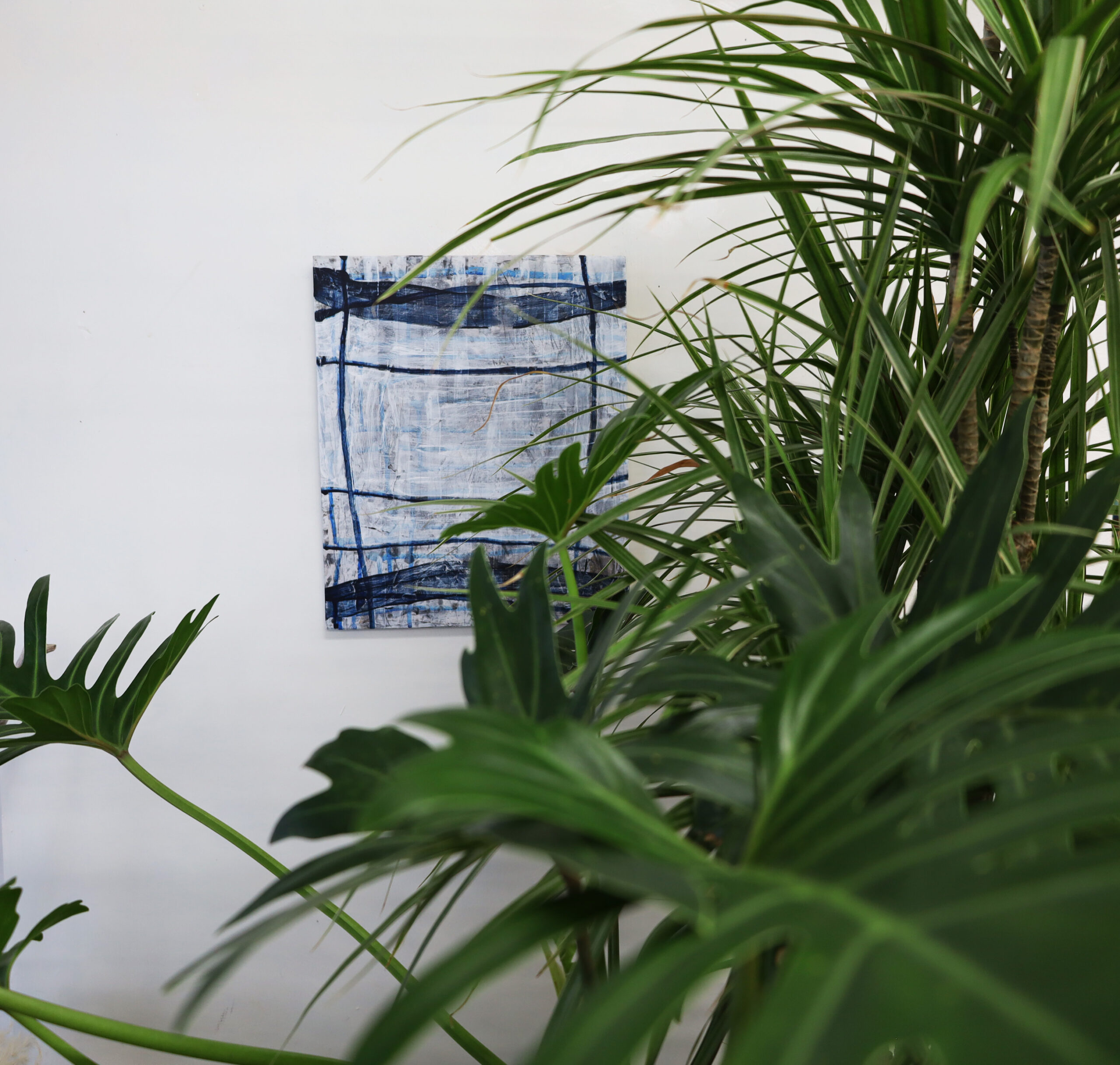 The original abstract painting 'Matrix Expansion' by Asahi Tanaka hanging on a white wall, styled with the lush green leaves of a houseplant in the foreground to create an organic modern and biophilic feel.